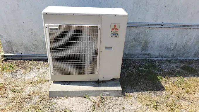 A white air conditioner is sitting on the ground in front of a white wall.