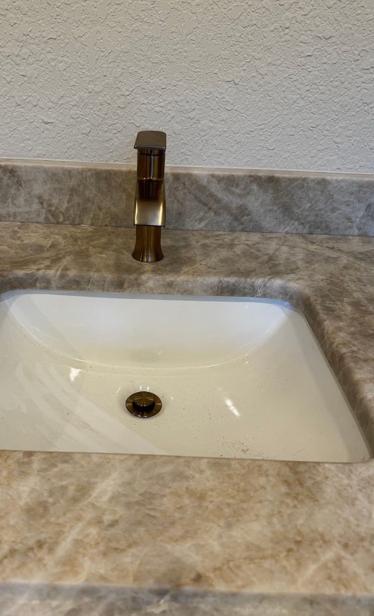 Prestige Plumbing LLC- a bathroom sink with a gold faucet on a marble counter top.