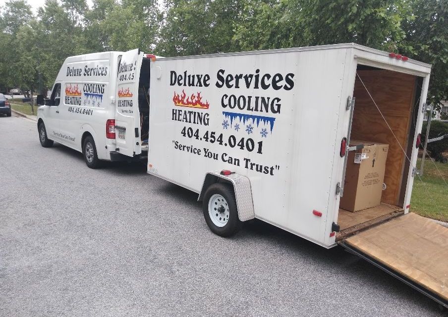 Two deluxe services vans are parked next to a trailer