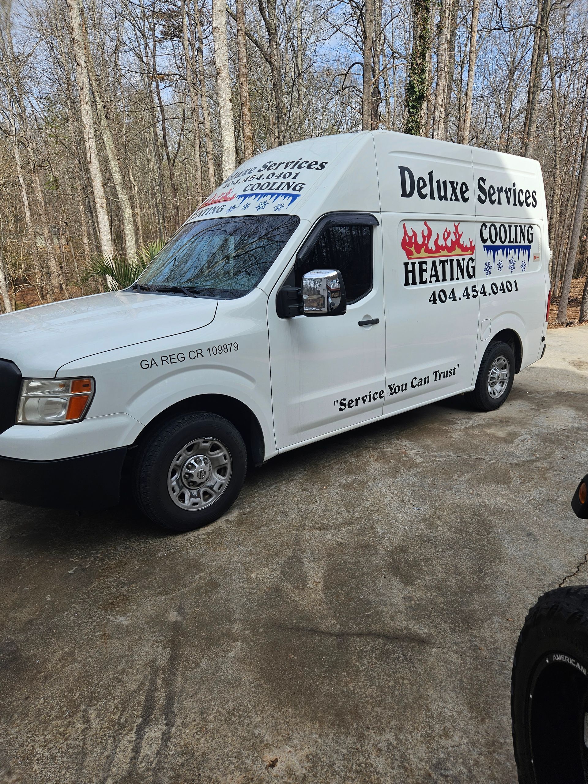 A white van is parked in a driveway with trees in the background.