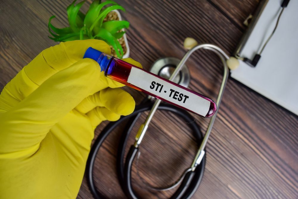 A hand in a yellow glove holds a blood vial labeled 