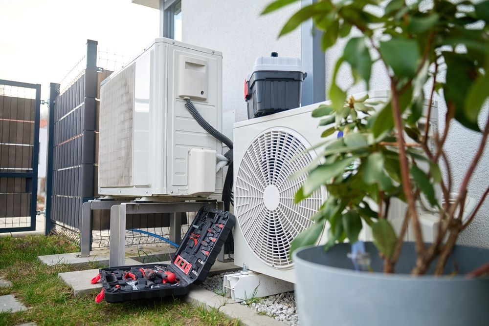 Outdoor HVAC units and a heat pump beside a fence, with a potted plant in the foreground.