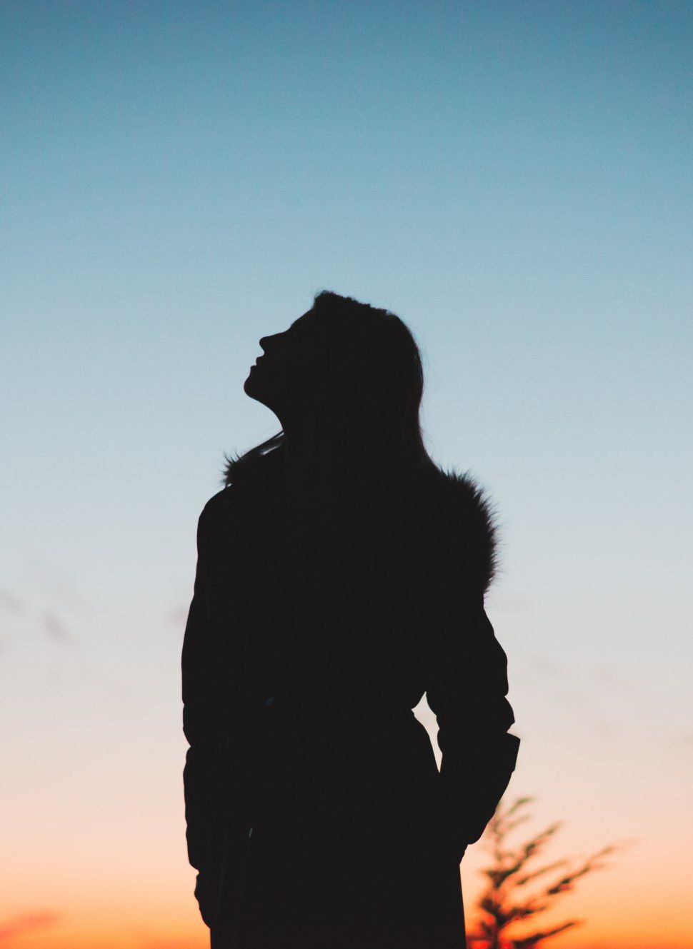 A silhouette of a woman in a fur coat looking up at the sky.