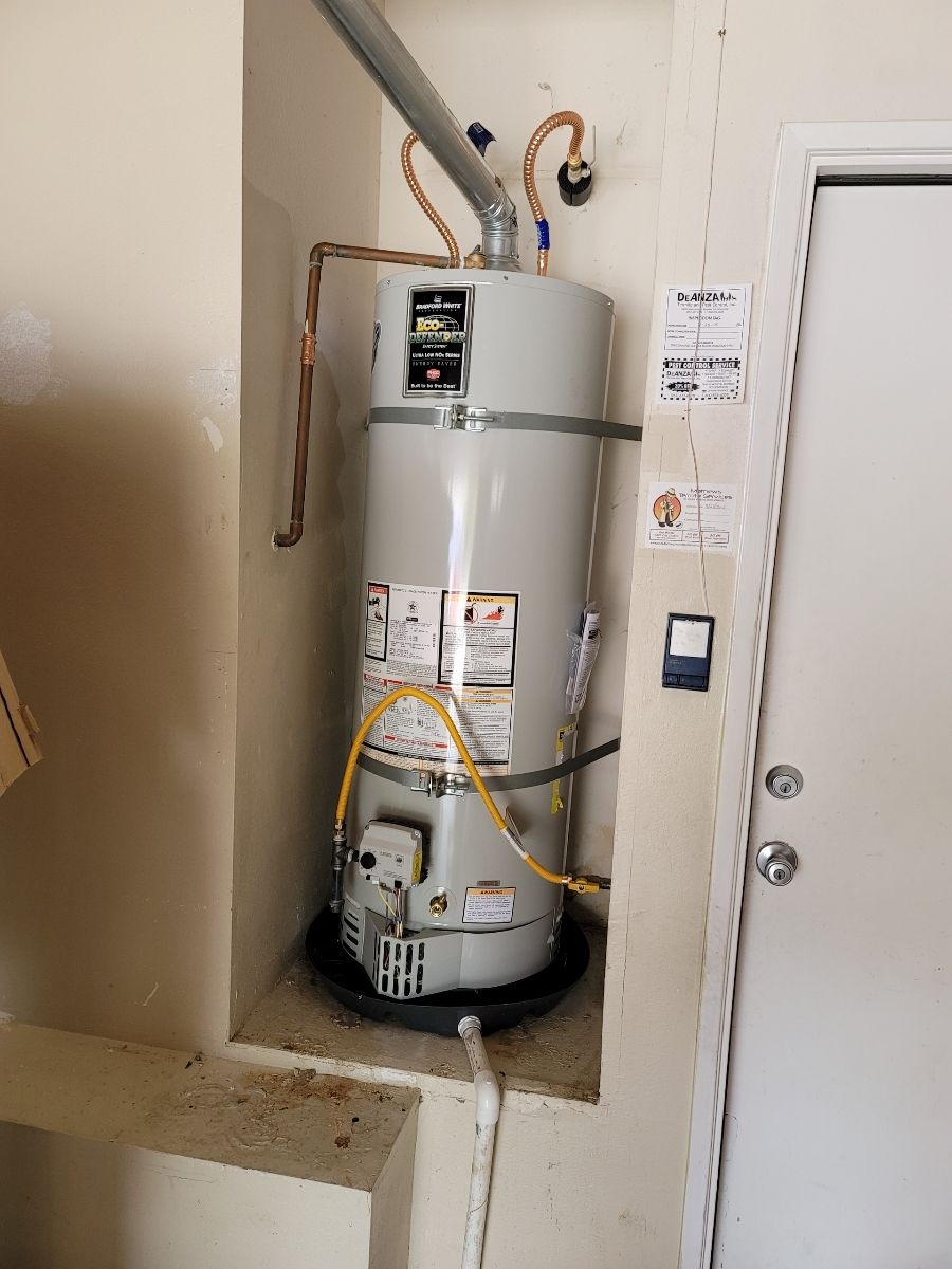 Traditional upright water heater tank installed in a utility room with visible piping.