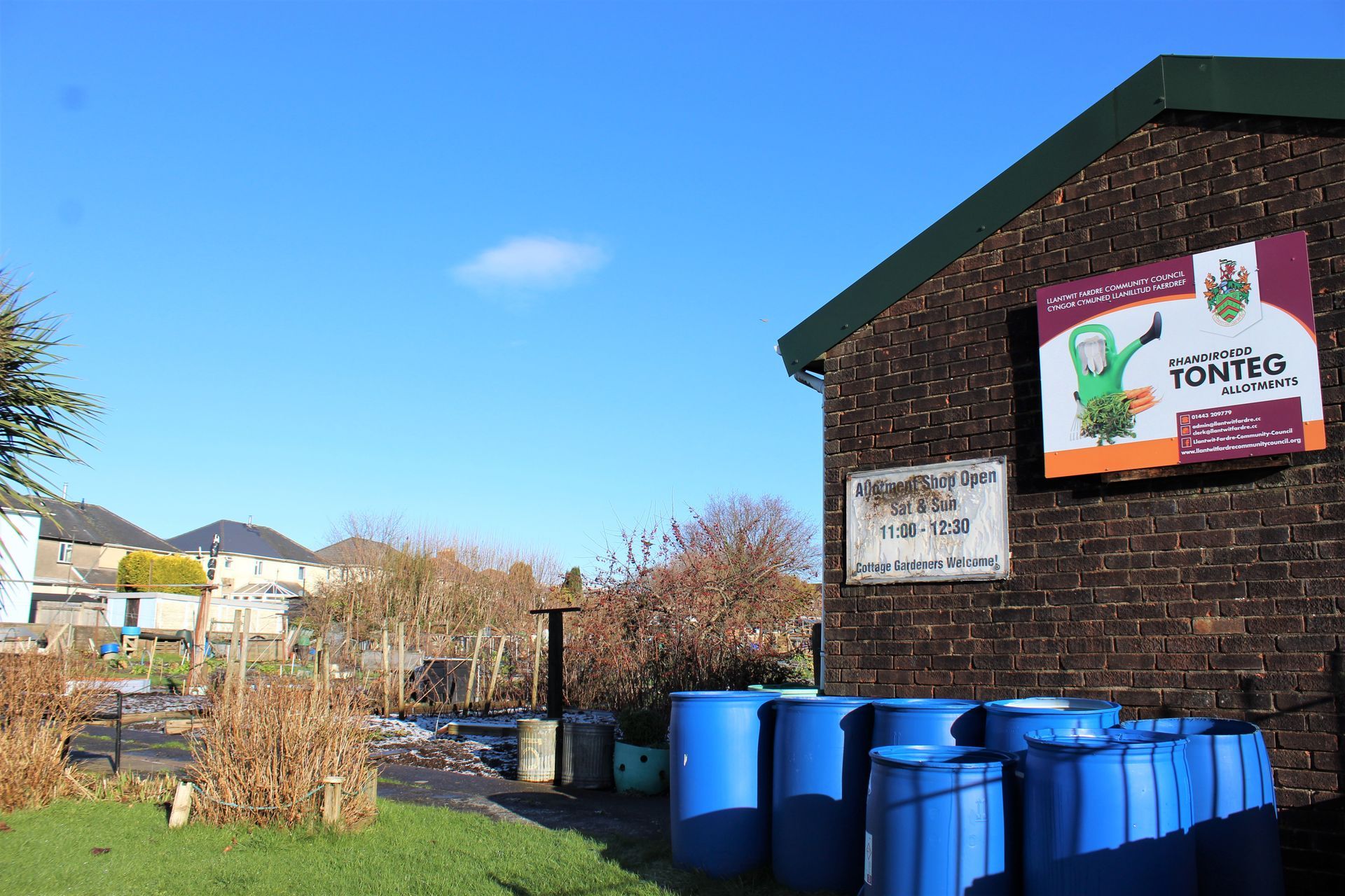 A garden with blue barrels, a brick building with a sign, and a clear blue sky.