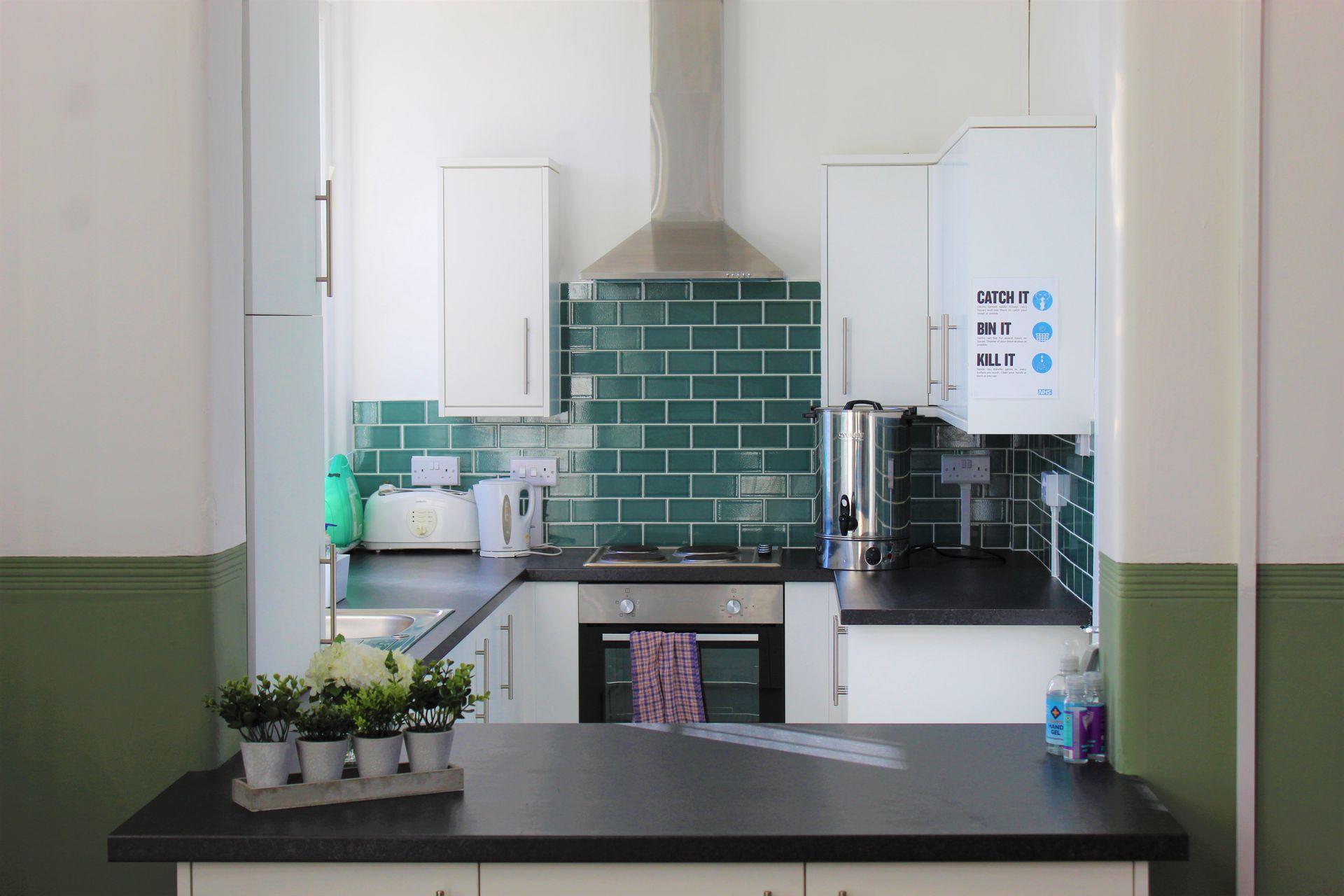 Kitchen with white cabinets, green tile backsplash, black countertops, and a green wall.