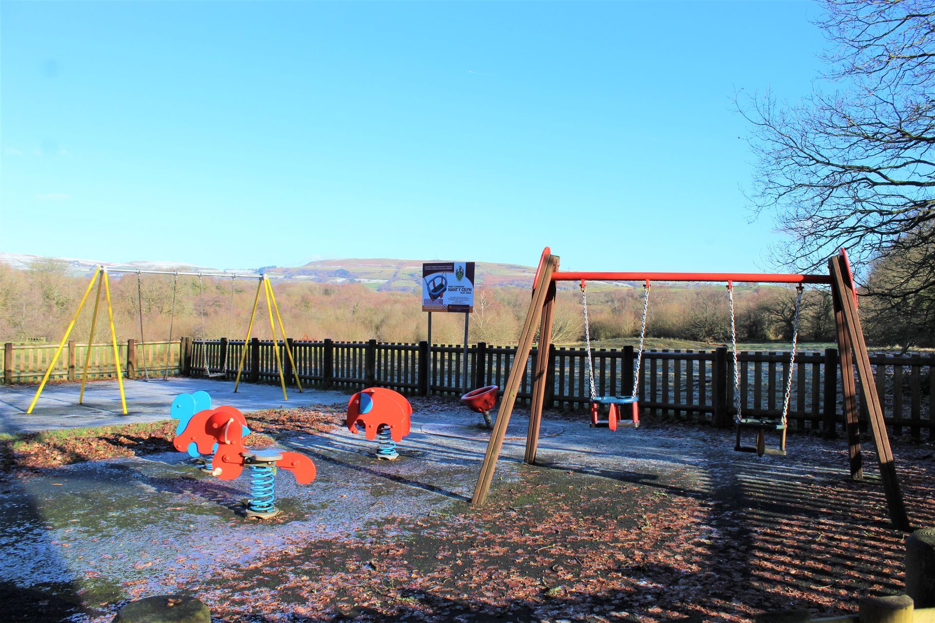 Playground with swings, spring riders, and fencing, on a sunny day.