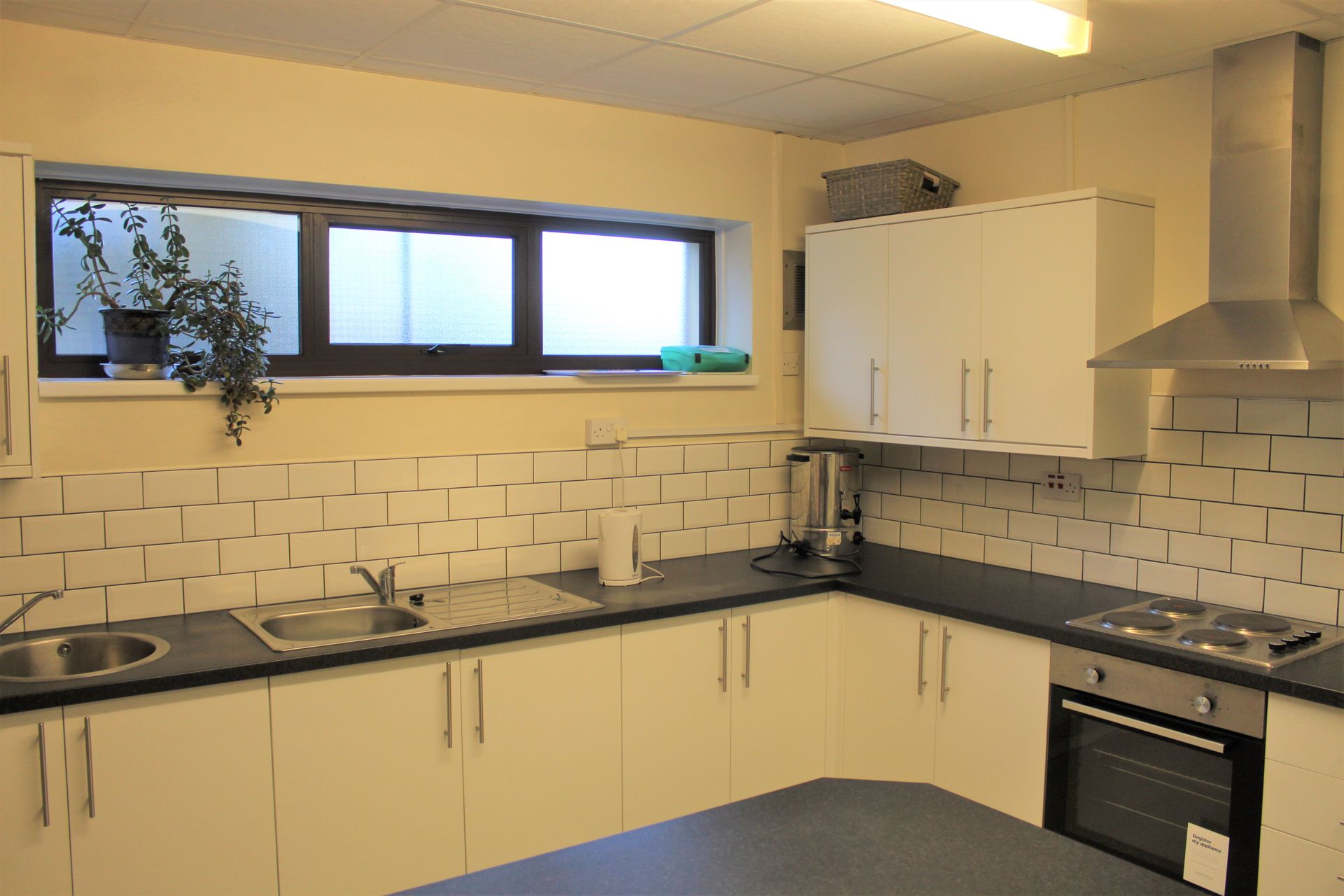 L-shaped kitchen with white cabinets, dark countertop, and stainless steel appliances. A window is in the back.
