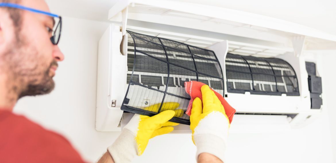 Man cleaning an air conditioner filter with yellow gloves and a red cloth.