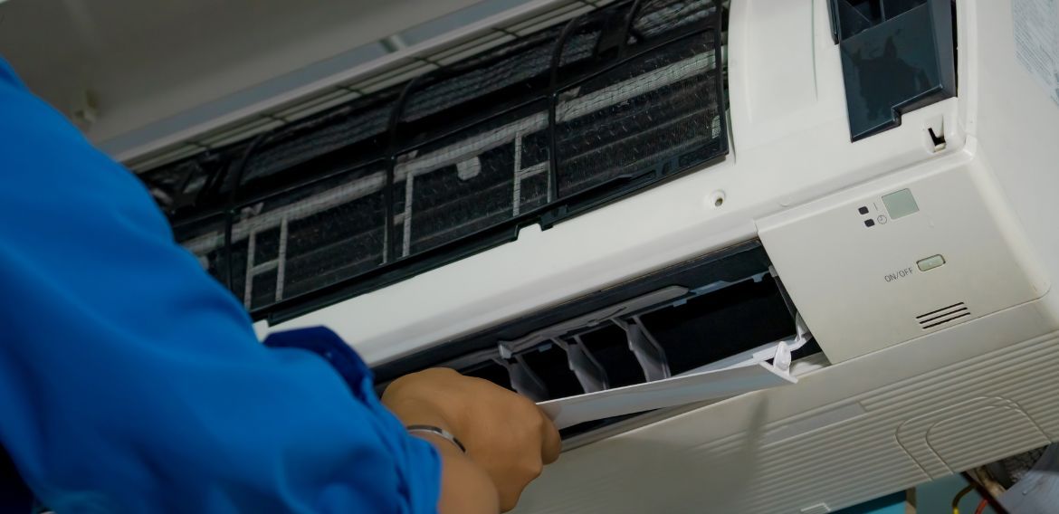 Person in blue shirt cleaning an air conditioner unit; indoors.