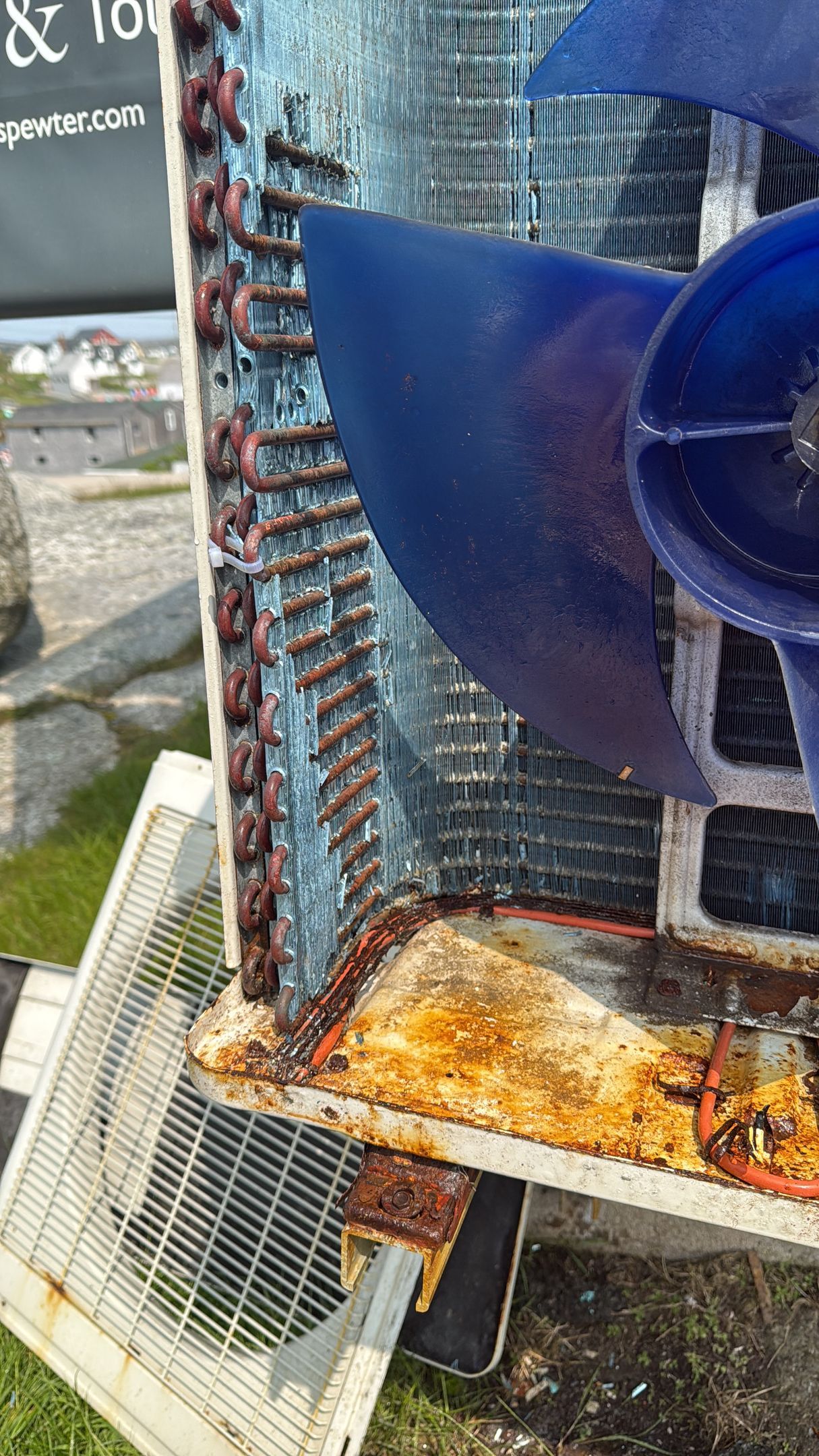 Corroded outdoor AC unit with blue fan. Rust and grime visible on coils.