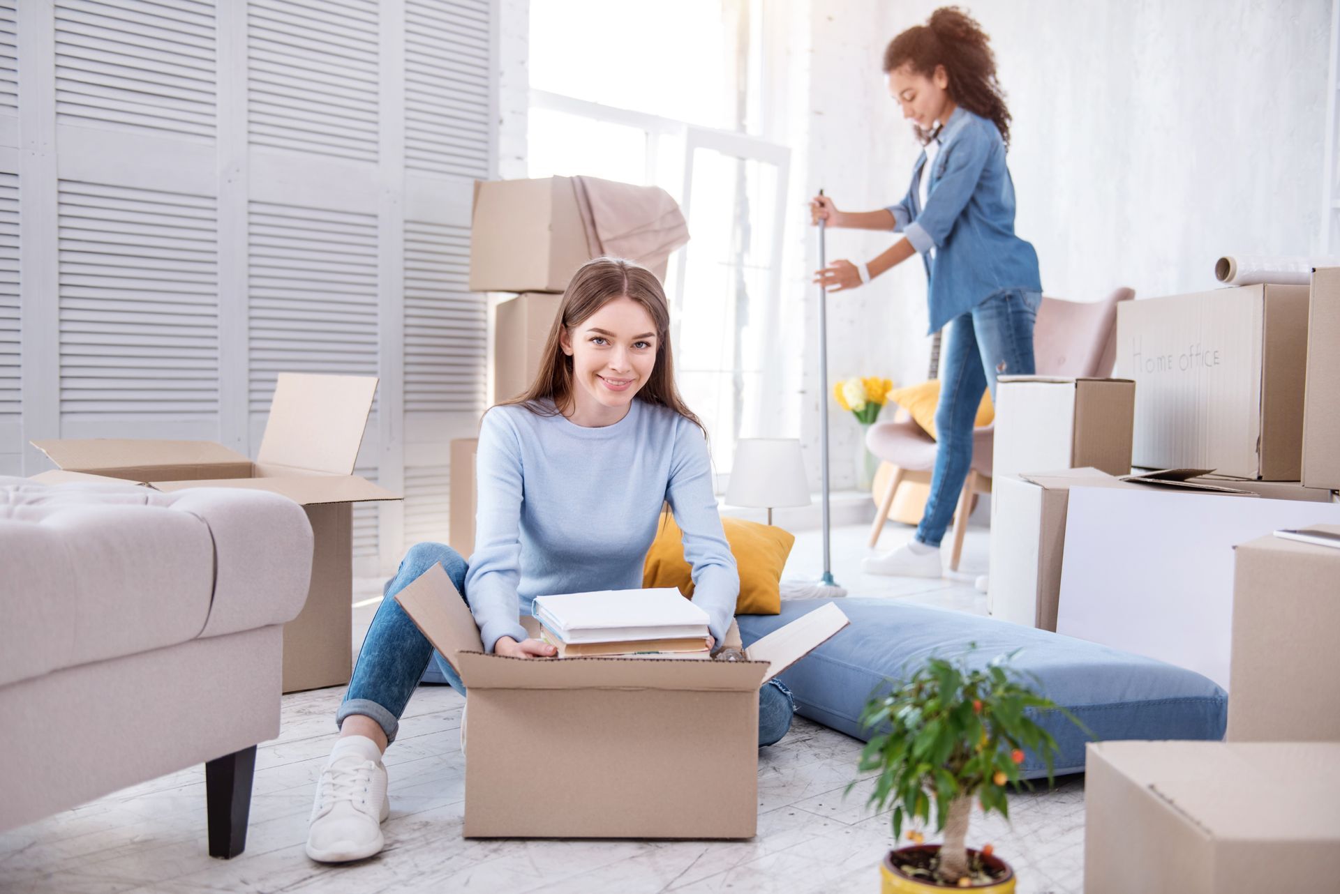 A woman is sitting on the floor in a living room holding a box.