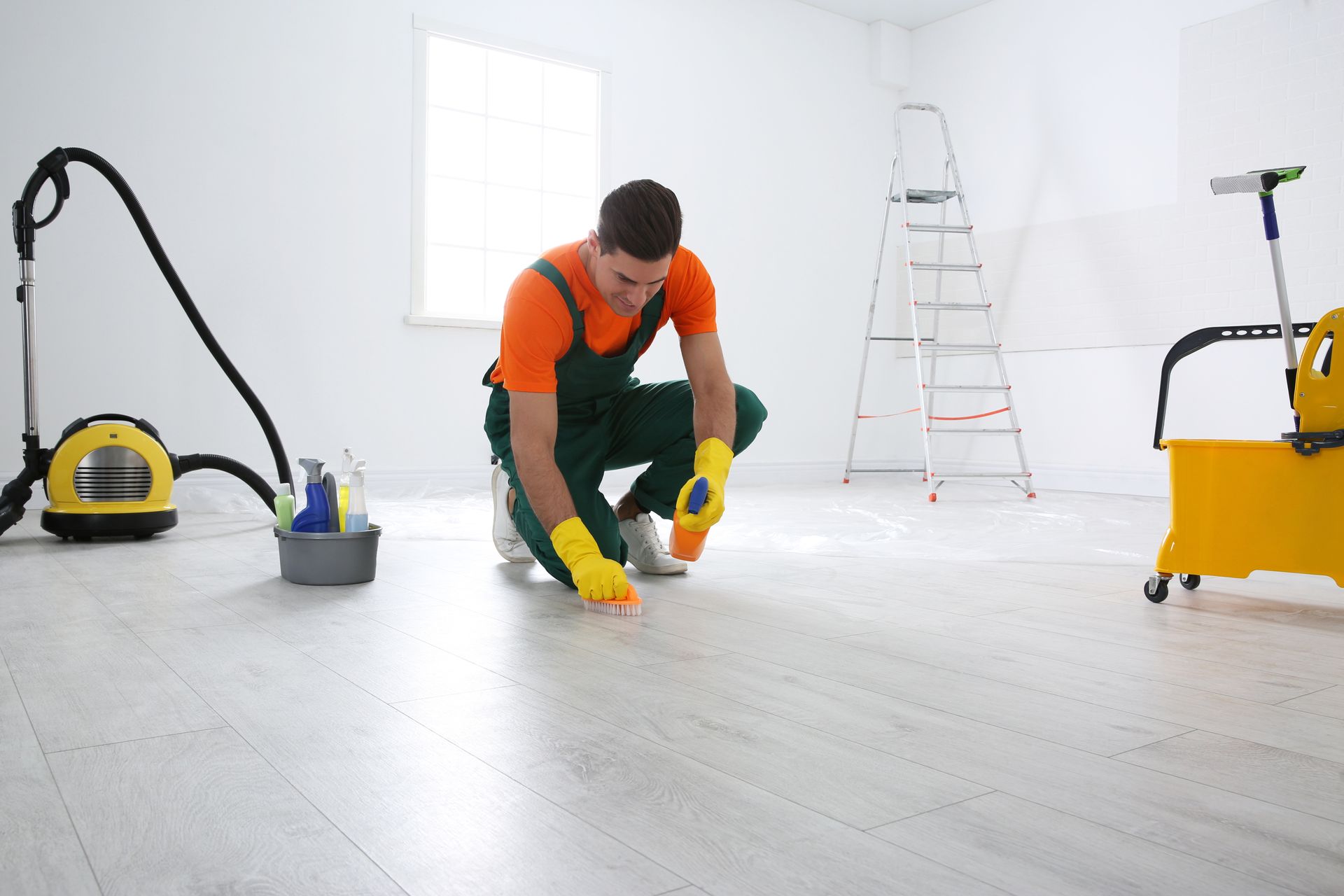 A man is cleaning the floor in a room with a vacuum cleaner and mop.
