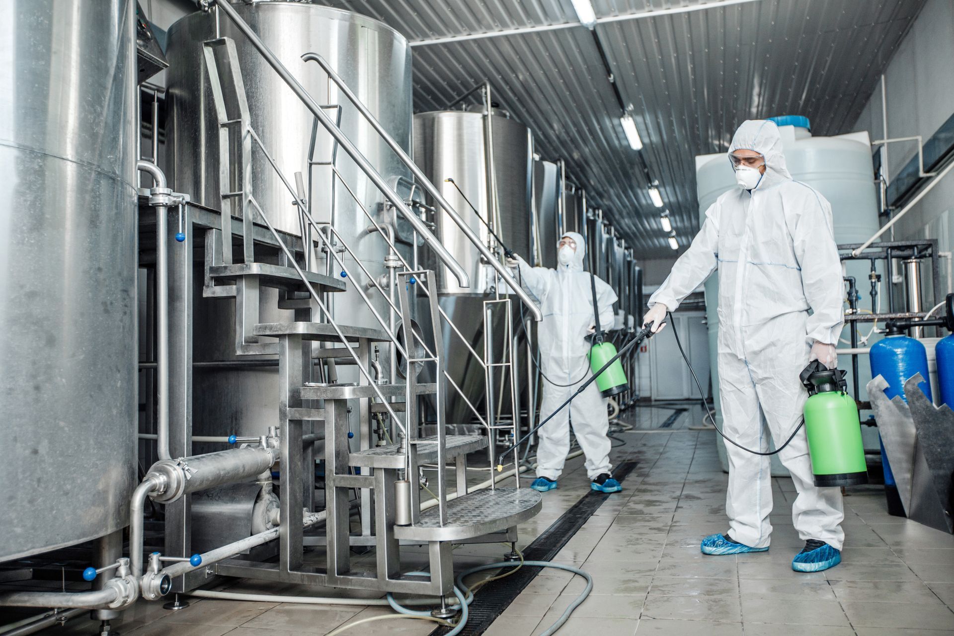Two men in protective suits are spraying chemicals in a factory.