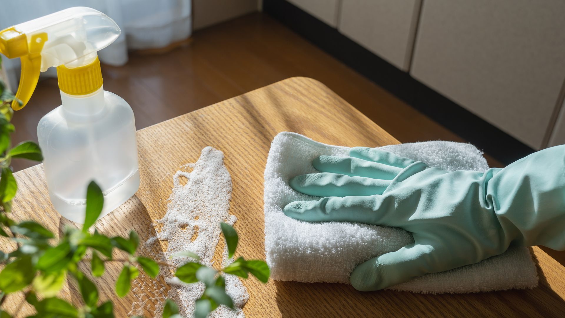 A person wearing gloves is cleaning a wooden table with a towel.