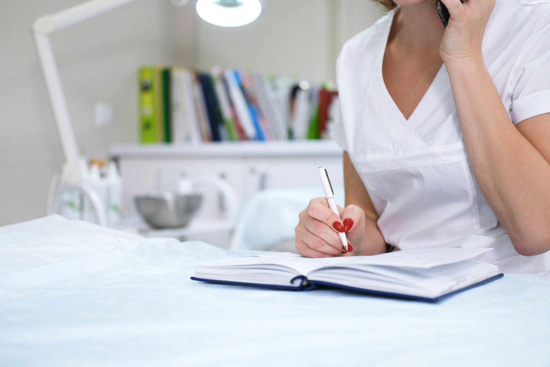 A woman is writing in a notebook while talking on a cell phone.