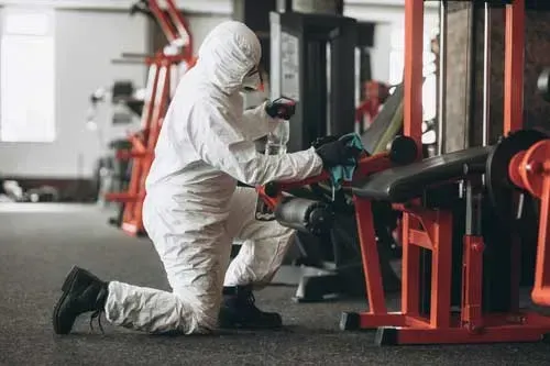 A man in a protective suit is cleaning a gym machine.