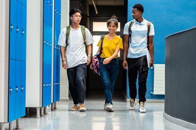 Three students walking through a bright blue school hallway with backpacks and books