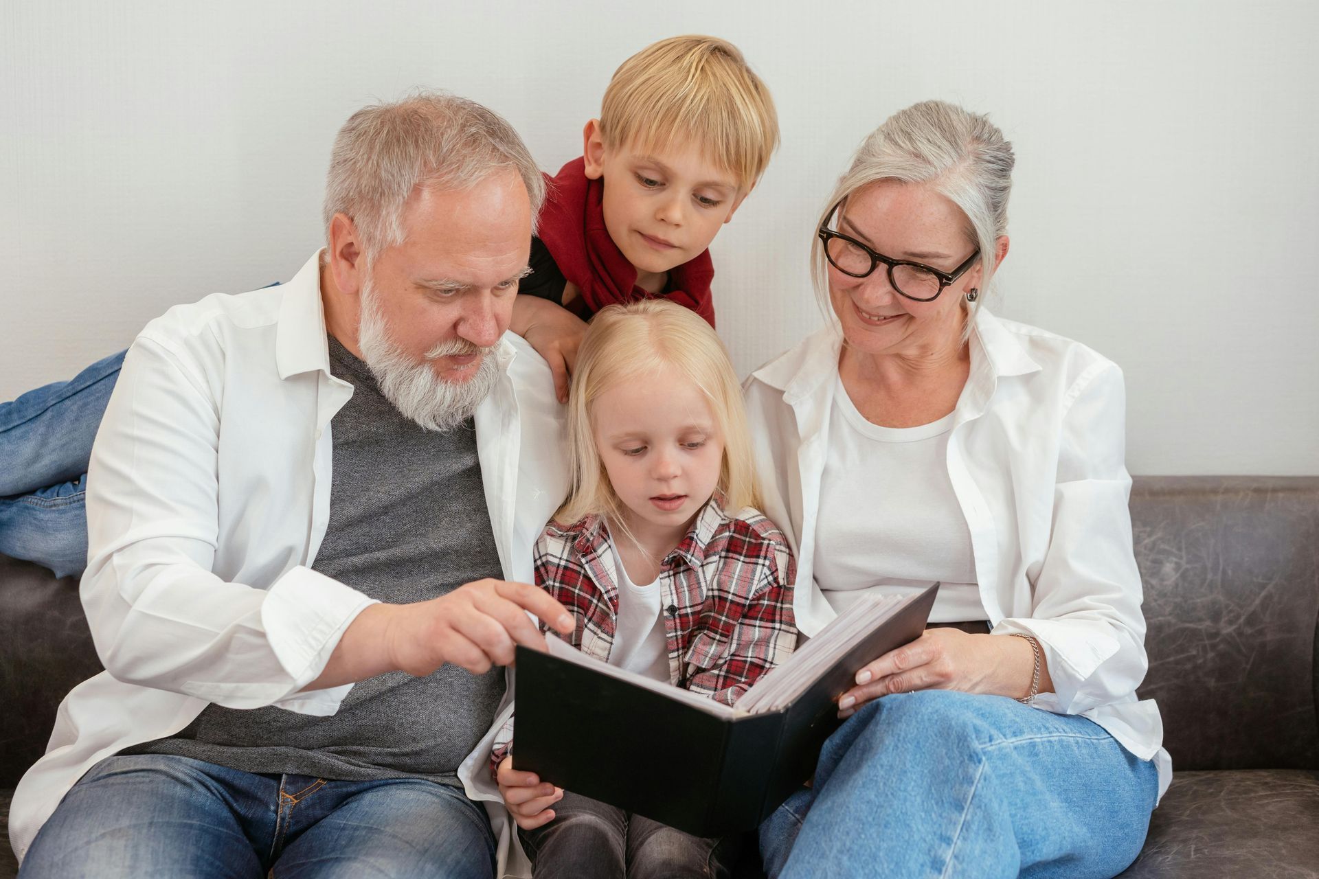 Grandparents read a book with their grandchildren on a couch; all looking intently.