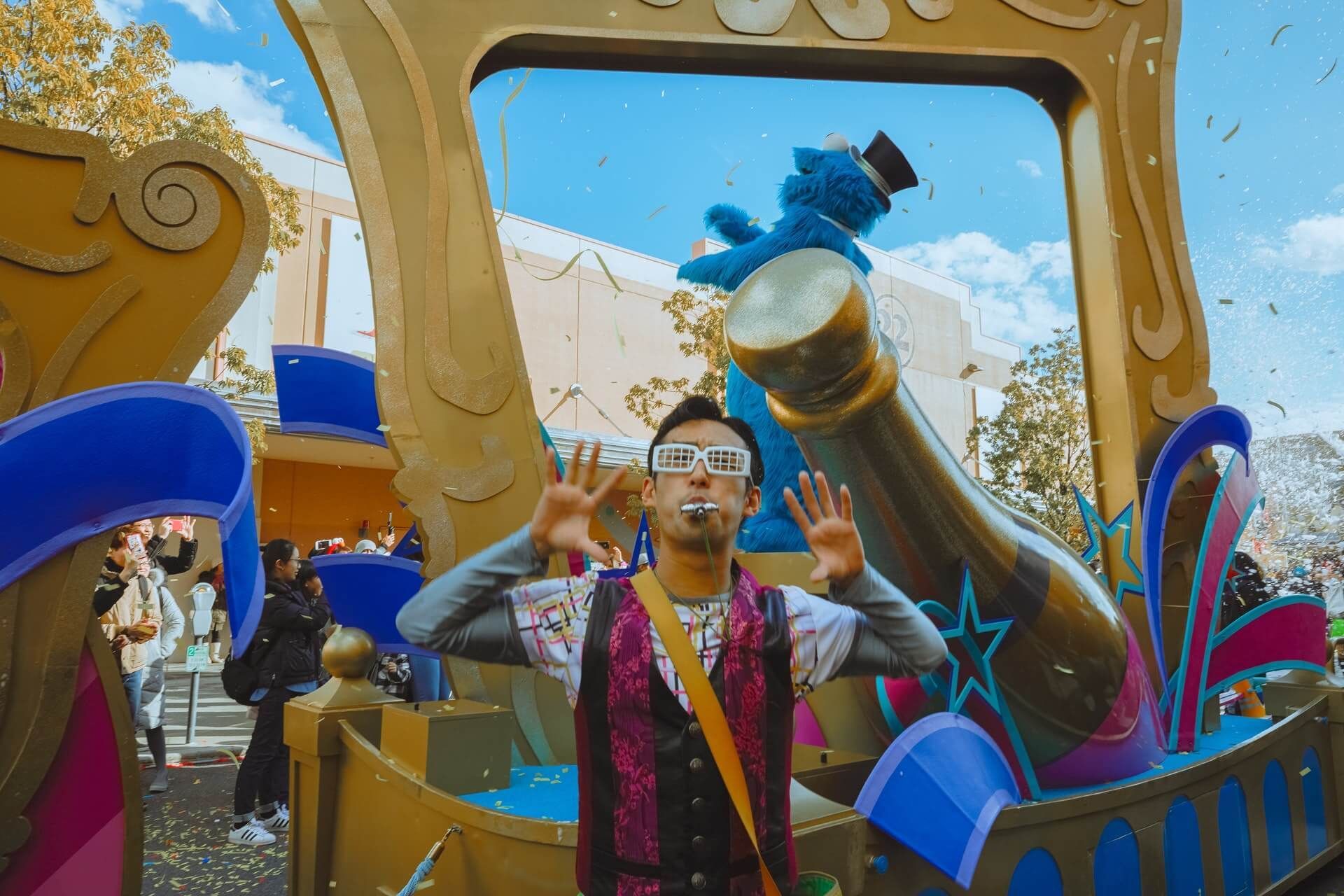 Man in costume with a celebratory pose in front of a colorful parade float with confetti.