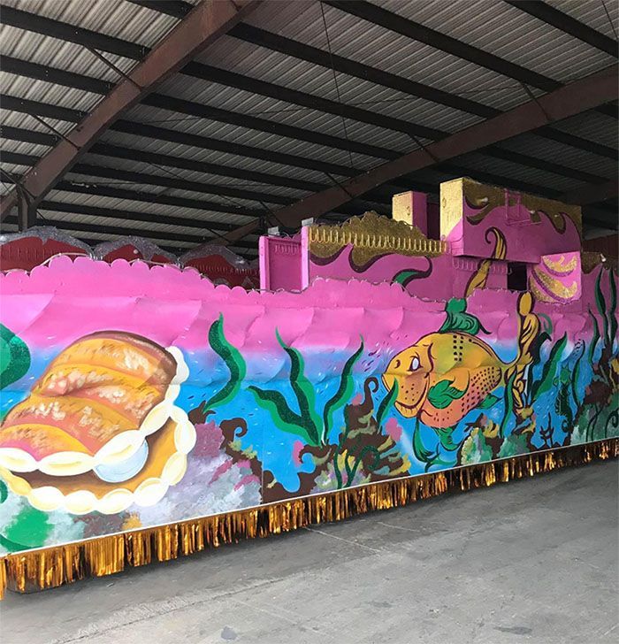 Pink and gold Mardi Gras parade float depicting an underwater scene with fish, shells, and seaweed.