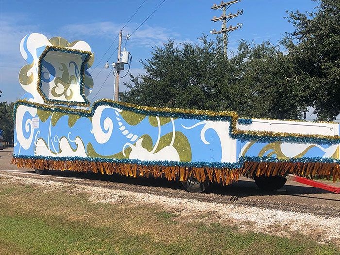 A parade float decorated in blue, white, and gold; parked on a road.
