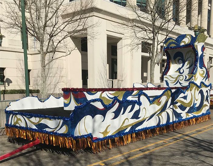Float with white, blue, and gold decorations, with fringed bottom, on a city street.