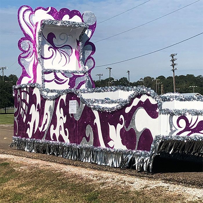 Mardi Gras float with white and purple swirls, silver tinsel trim, and a raised platform.