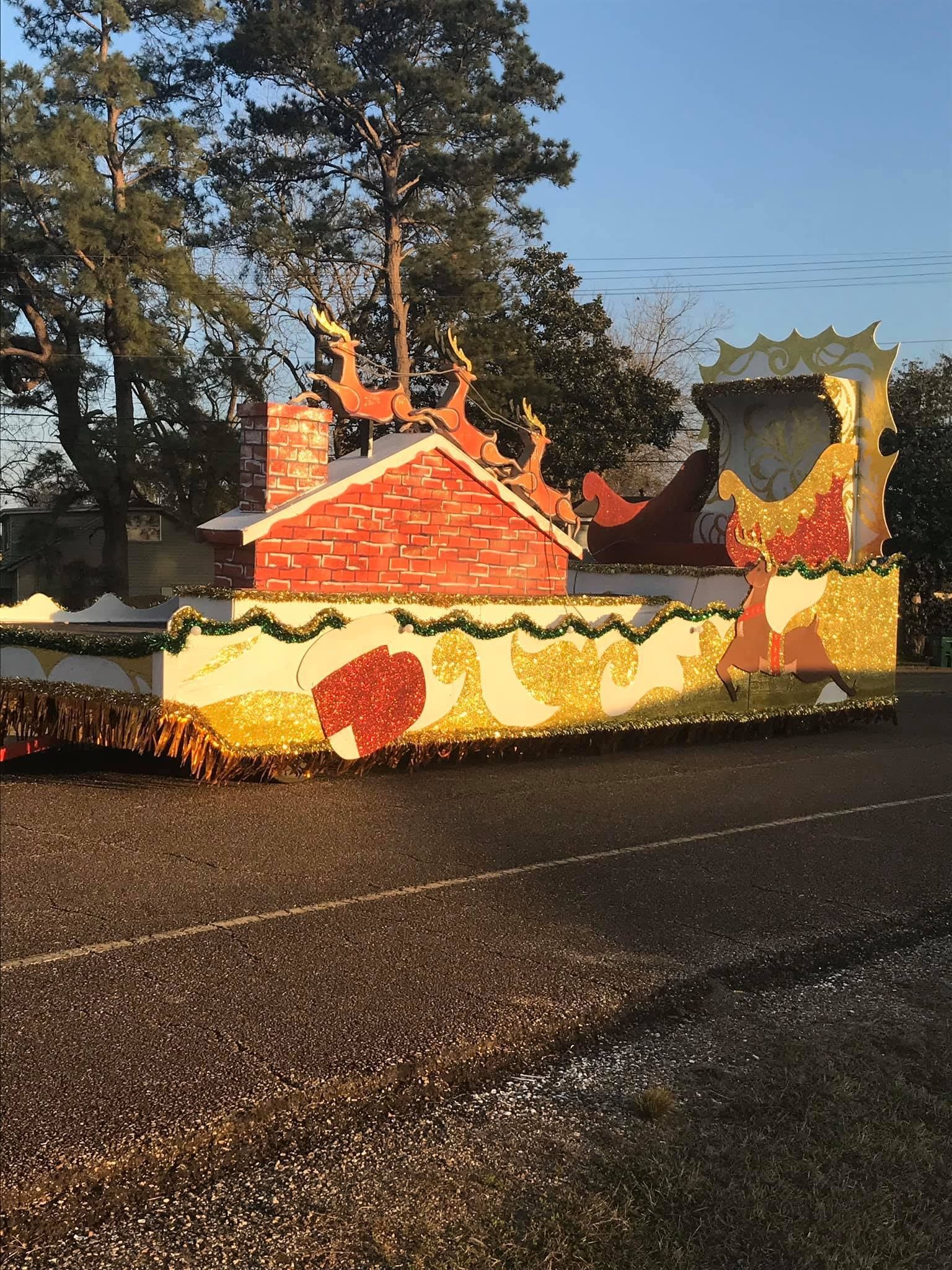 Christmas parade float with a red brick house, reindeer on the chimney, and colorful decorations.