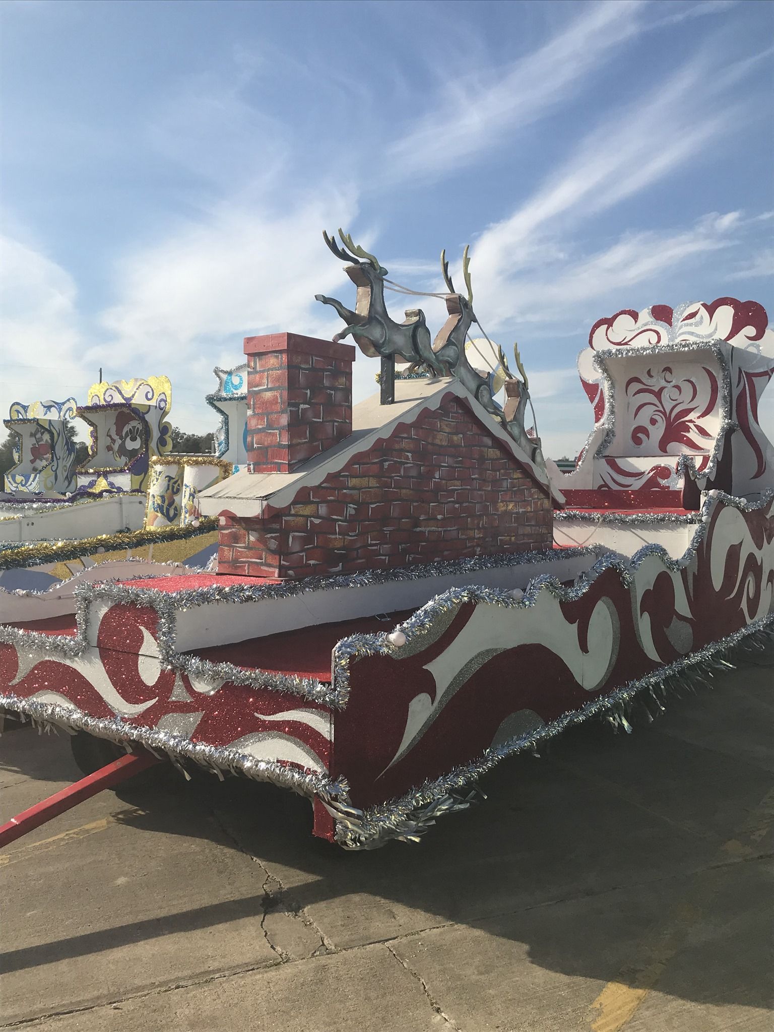 Parade float with Santa's sleigh design, featuring reindeer, a chimney, and red and white decorations.