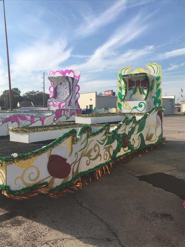 Mardi Gras parade floats decorated with pink and green embellishments, parked on concrete.