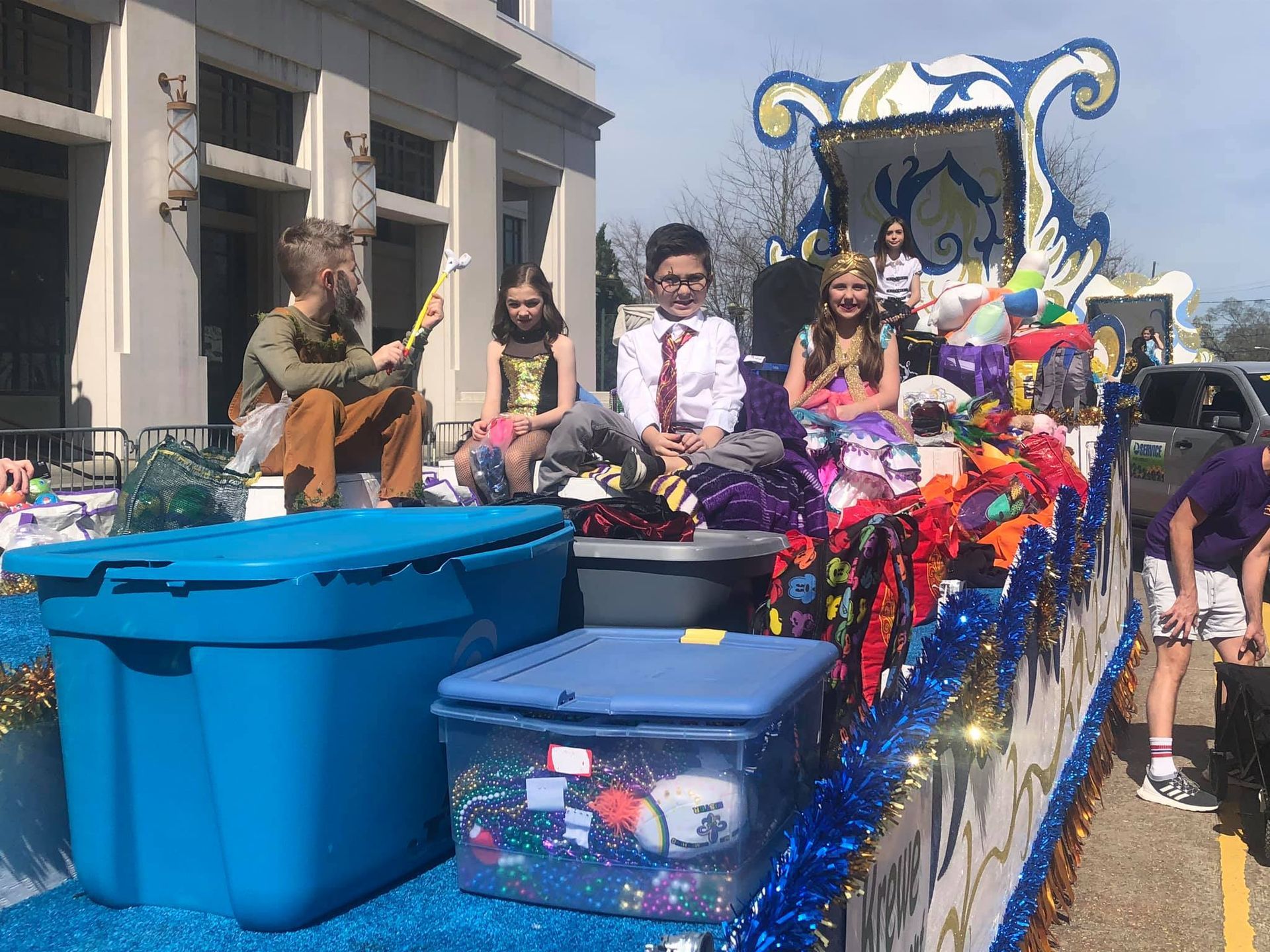 Children on a parade float, decorated with blue and gold, holding toys.