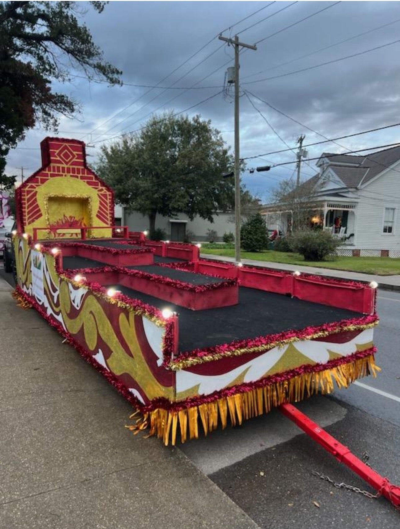 A decorated parade float with red, gold, and white accents, featuring a stage-like platform with a chimney structure.
