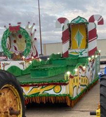 A Christmas-themed parade float with candy cane decorations, a green wreath, and decorative trim.