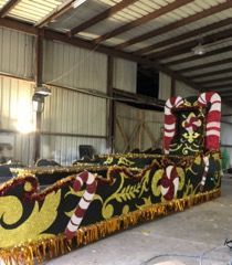 A colorful Christmas float with candy cane accents, inside a large building.