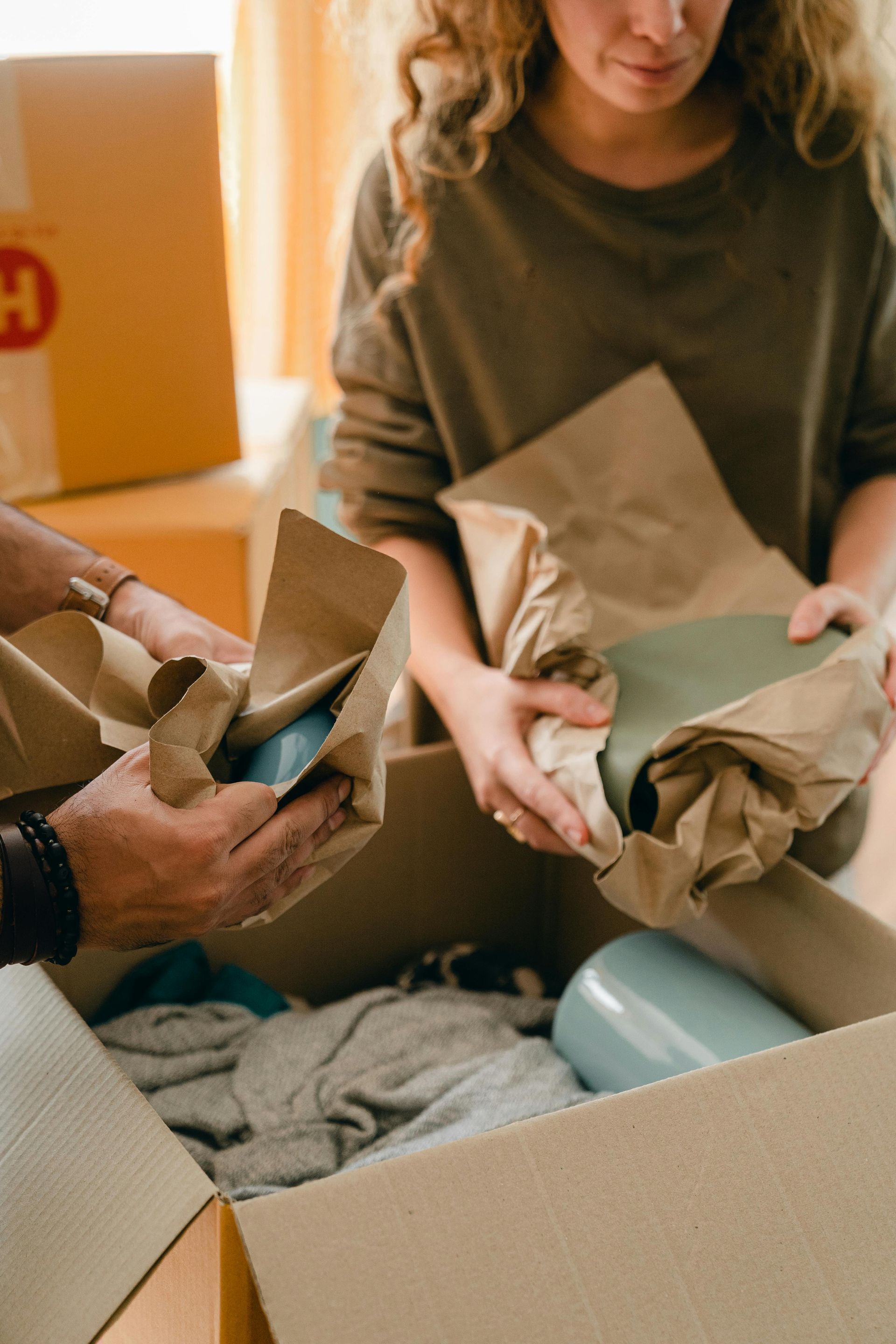 A man and a woman are opening a cardboard box filled with clothes.