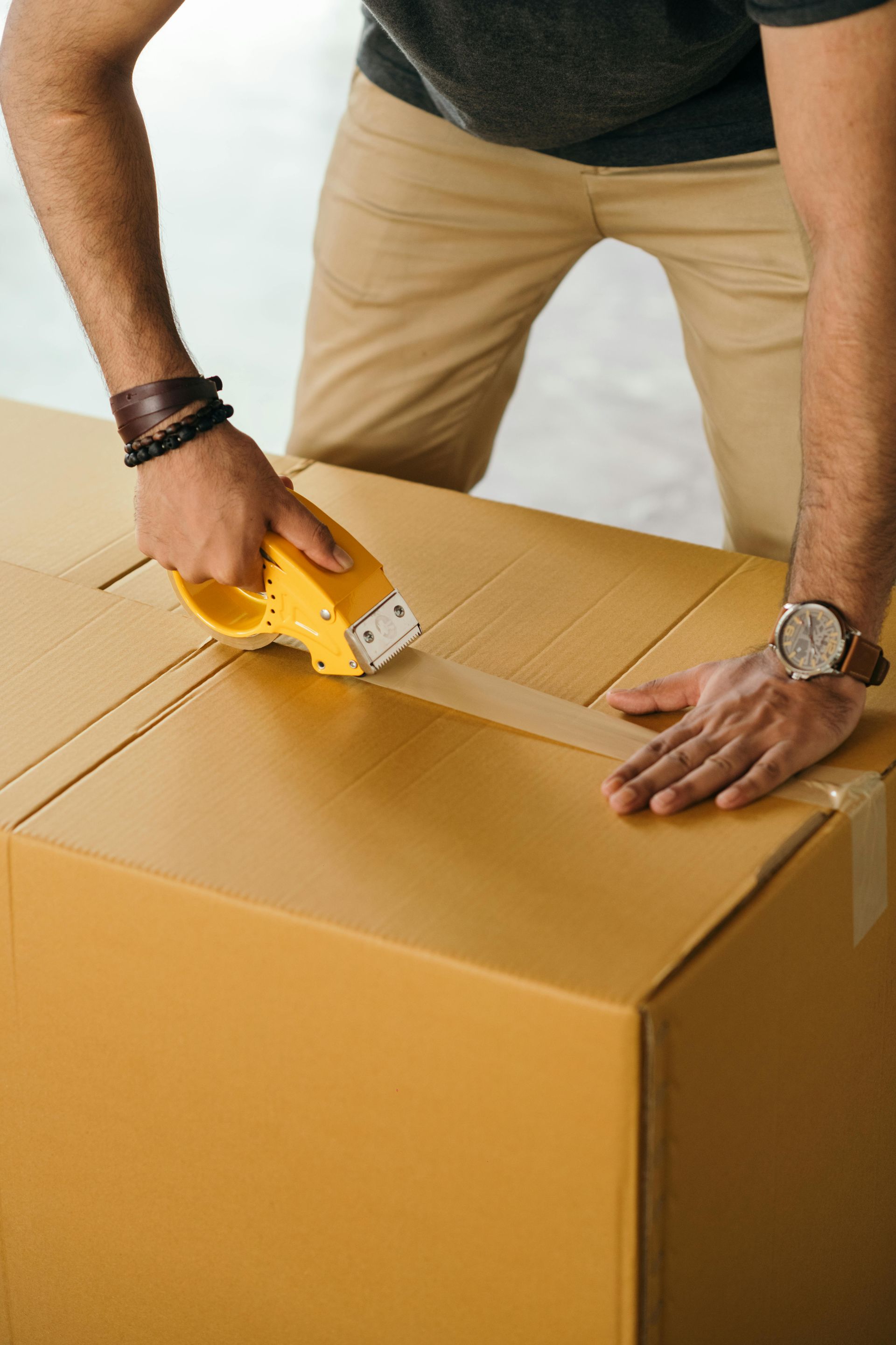 A man is taping a cardboard box with tape.