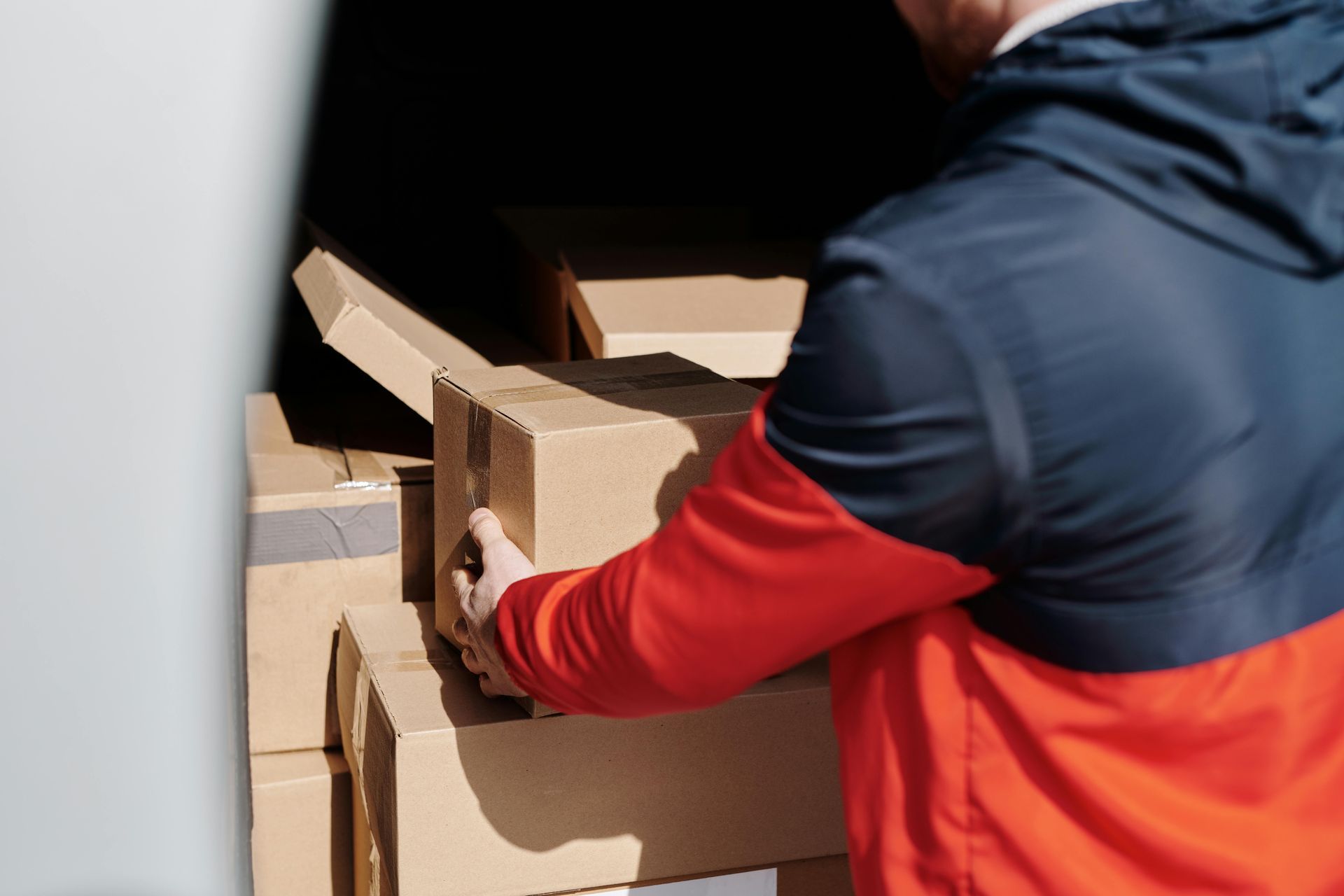 A man in a red and blue jacket is opening a cardboard box.