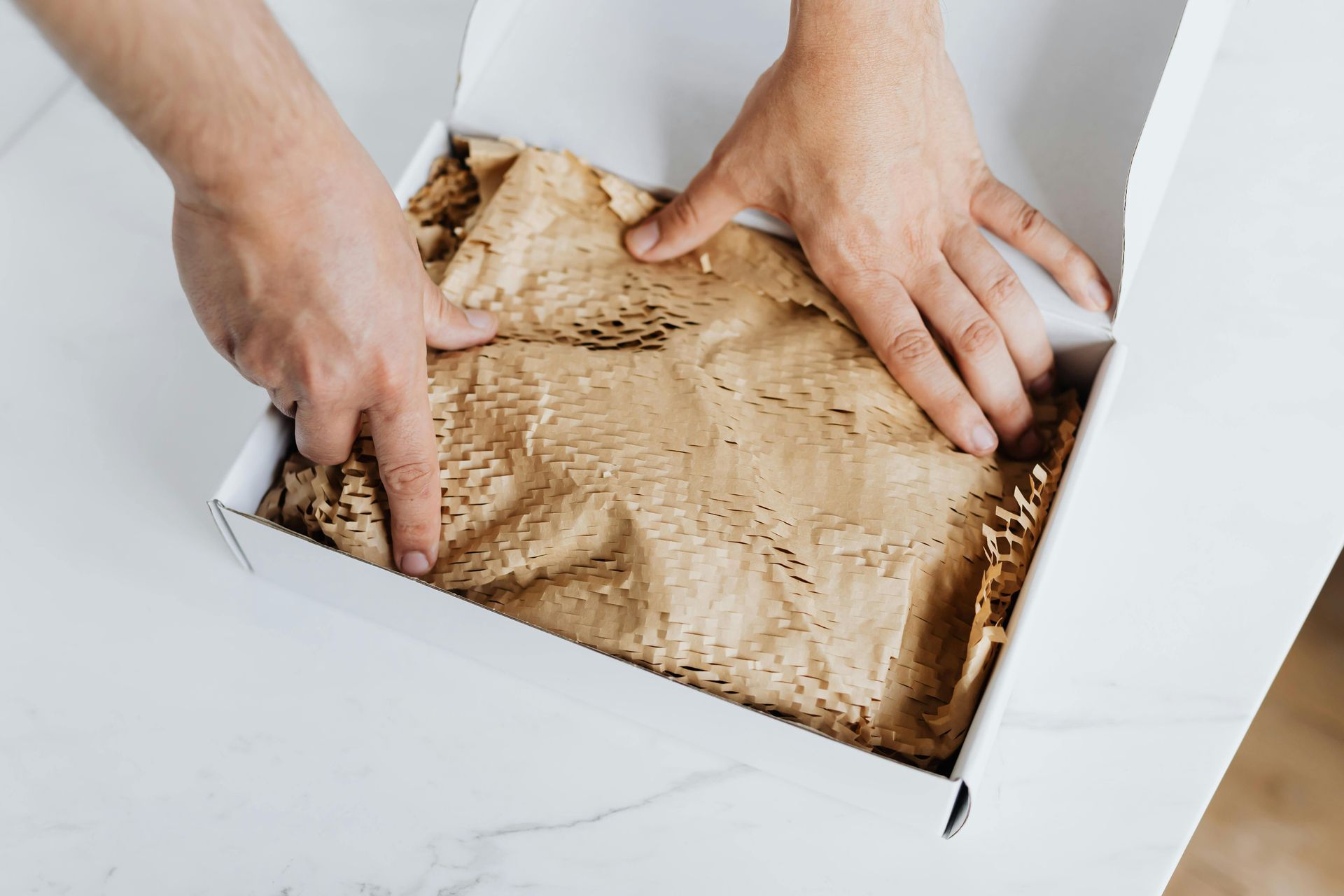 A person is packing a box with brown paper and shredded paper.