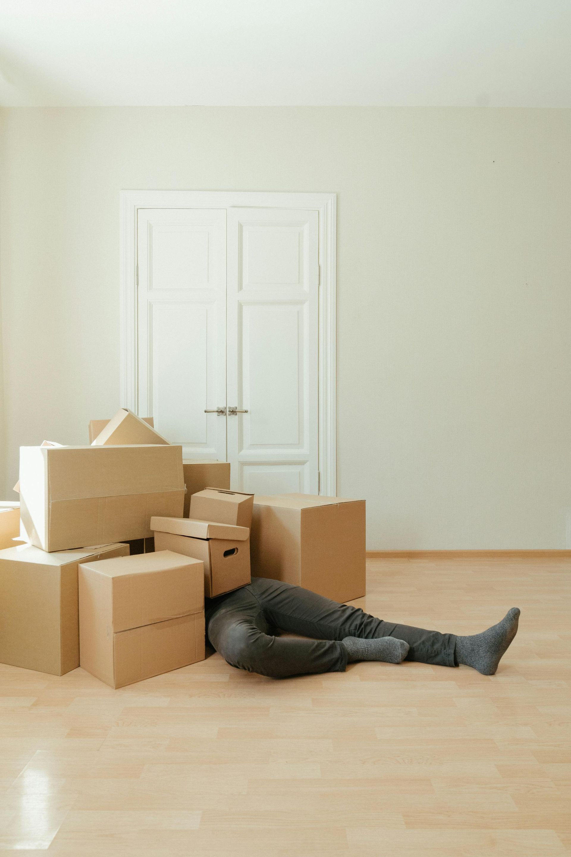 A man is laying on the floor in front of a pile of cardboard boxes.