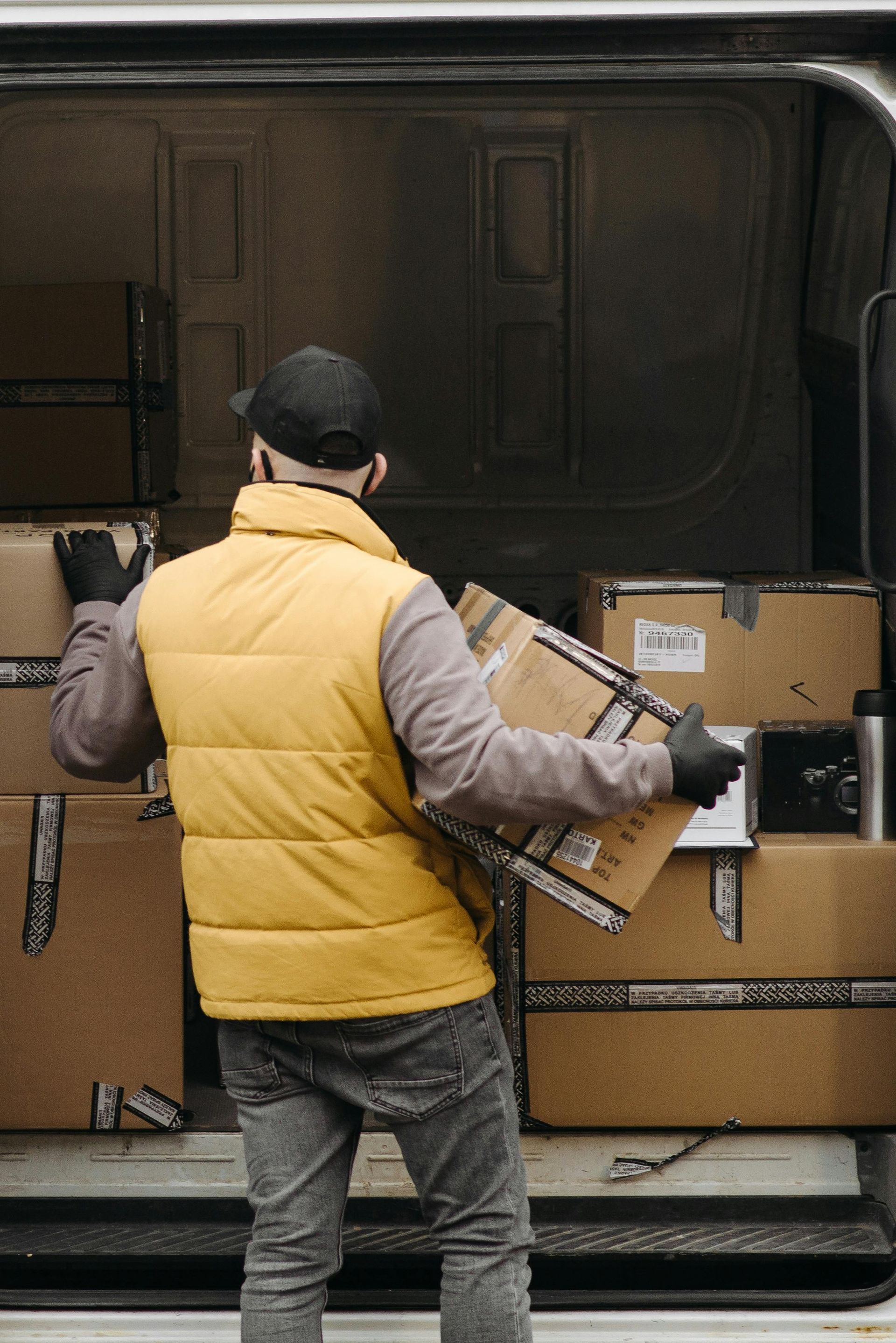 A man in a yellow vest is loading boxes into a van.