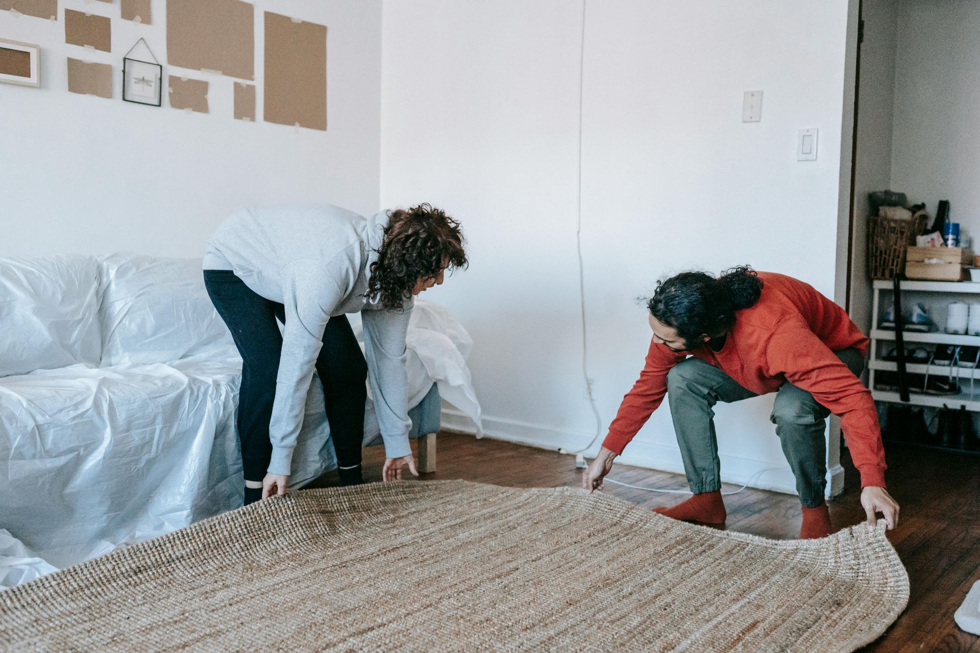 Two people are laying a rug on the floor in a living room.