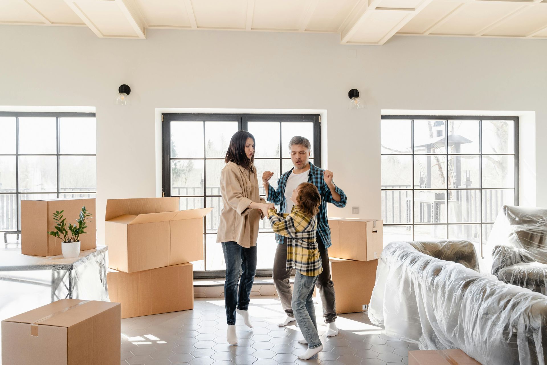 A family is dancing in their new home surrounded by cardboard boxes.