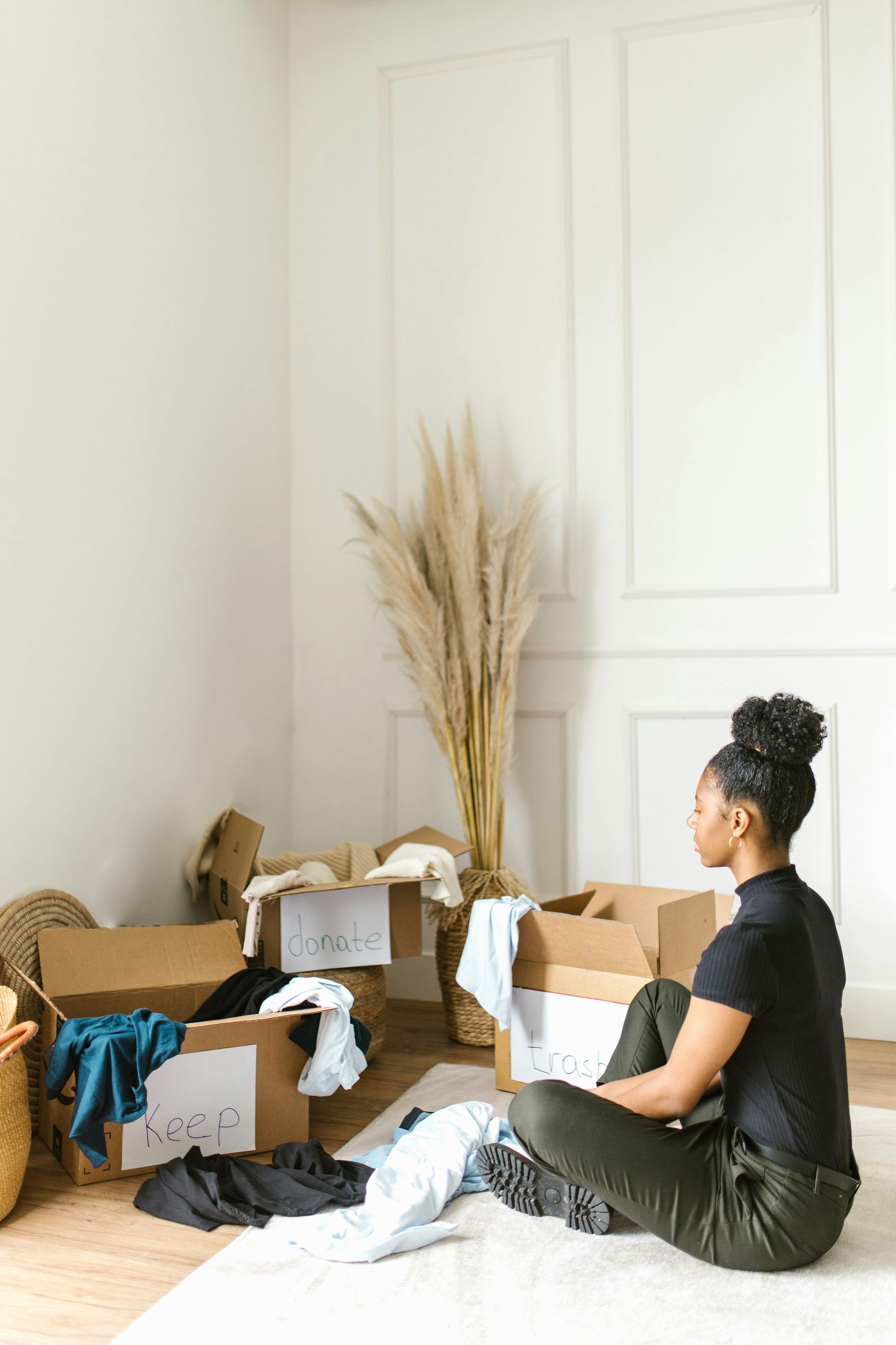 A woman is sitting on the floor in a room filled with cardboard boxes.