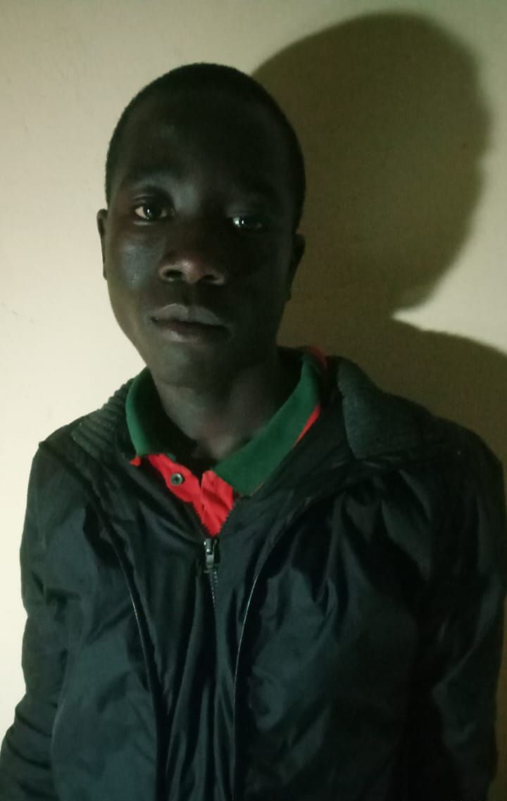 Young child in blue shirt, outdoors, looking at the camera.