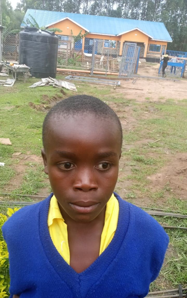 A young man with short hair in a blue hoodie stands outside. The sky is bright, with trees in the background.