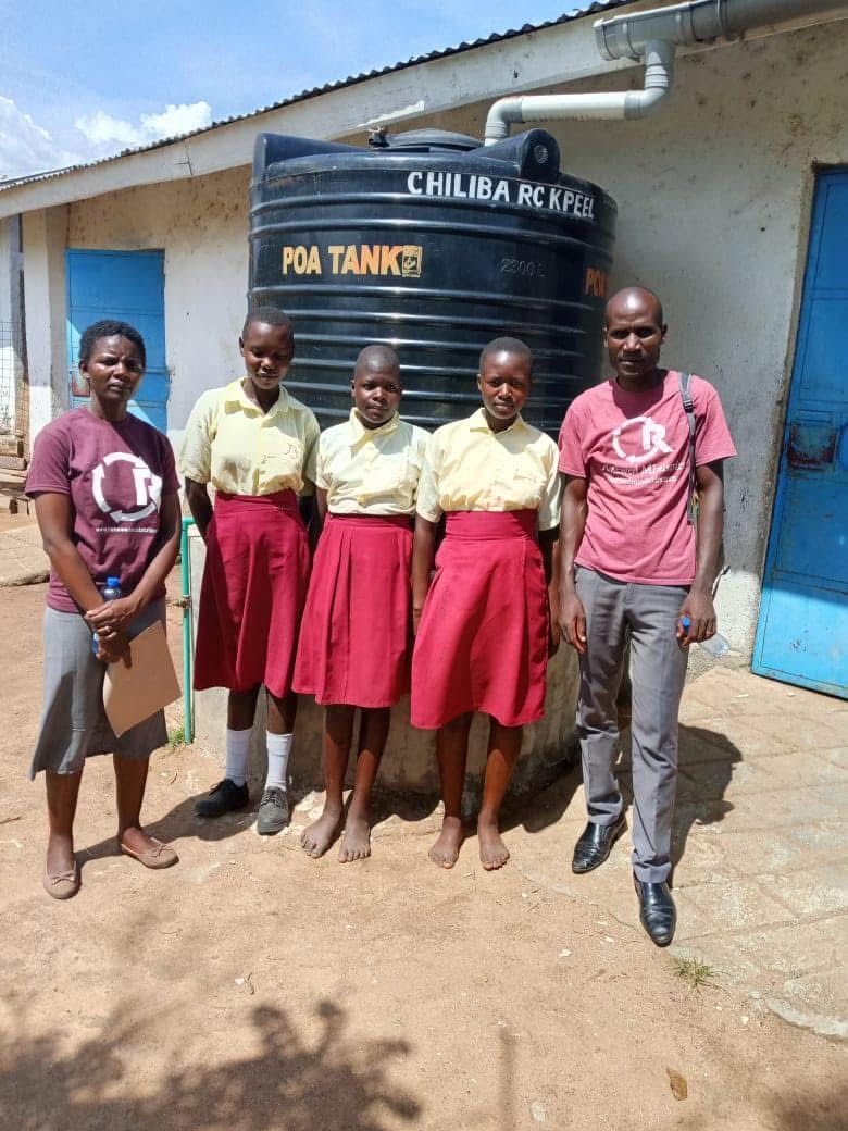 Group of people posing by a water tank at a building in Chiliba.