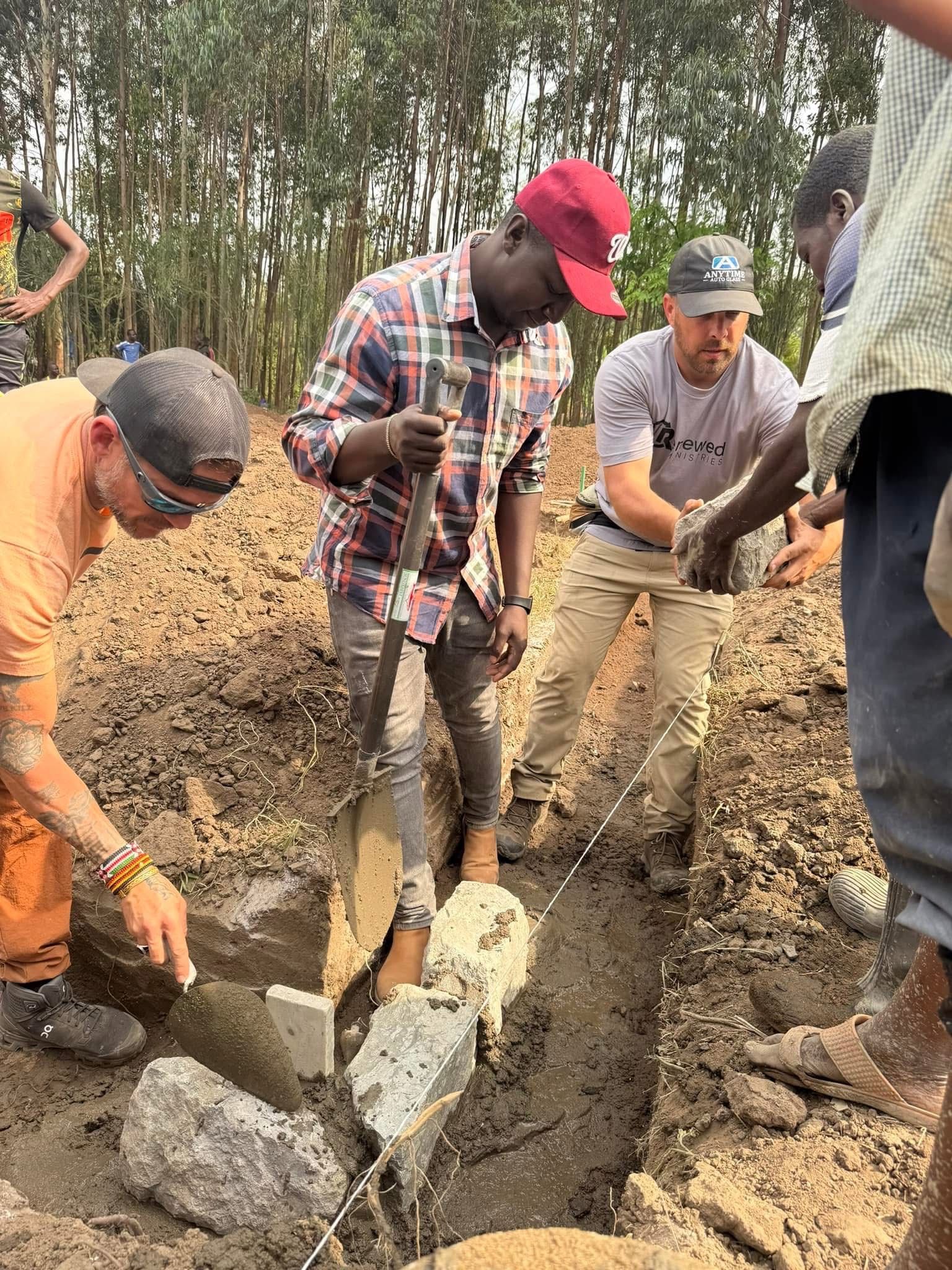 People laying stones in a ditch, possibly for construction, outdoors. They are muddy and focused on the work.