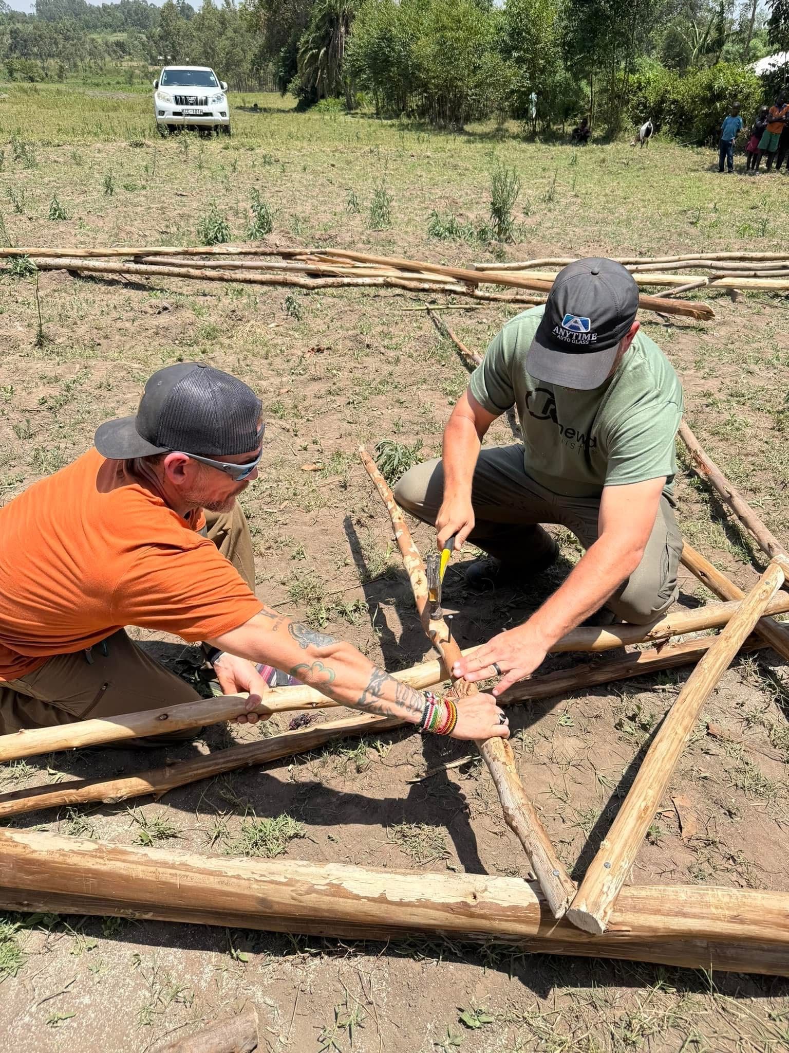 Two men assembling wooden frame outdoors on a sunny day.