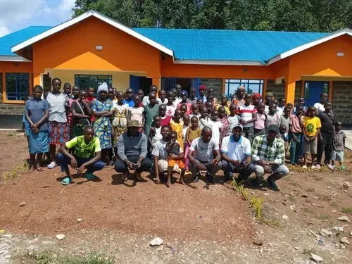 Group of people standing in front of an orange building with blue roof.